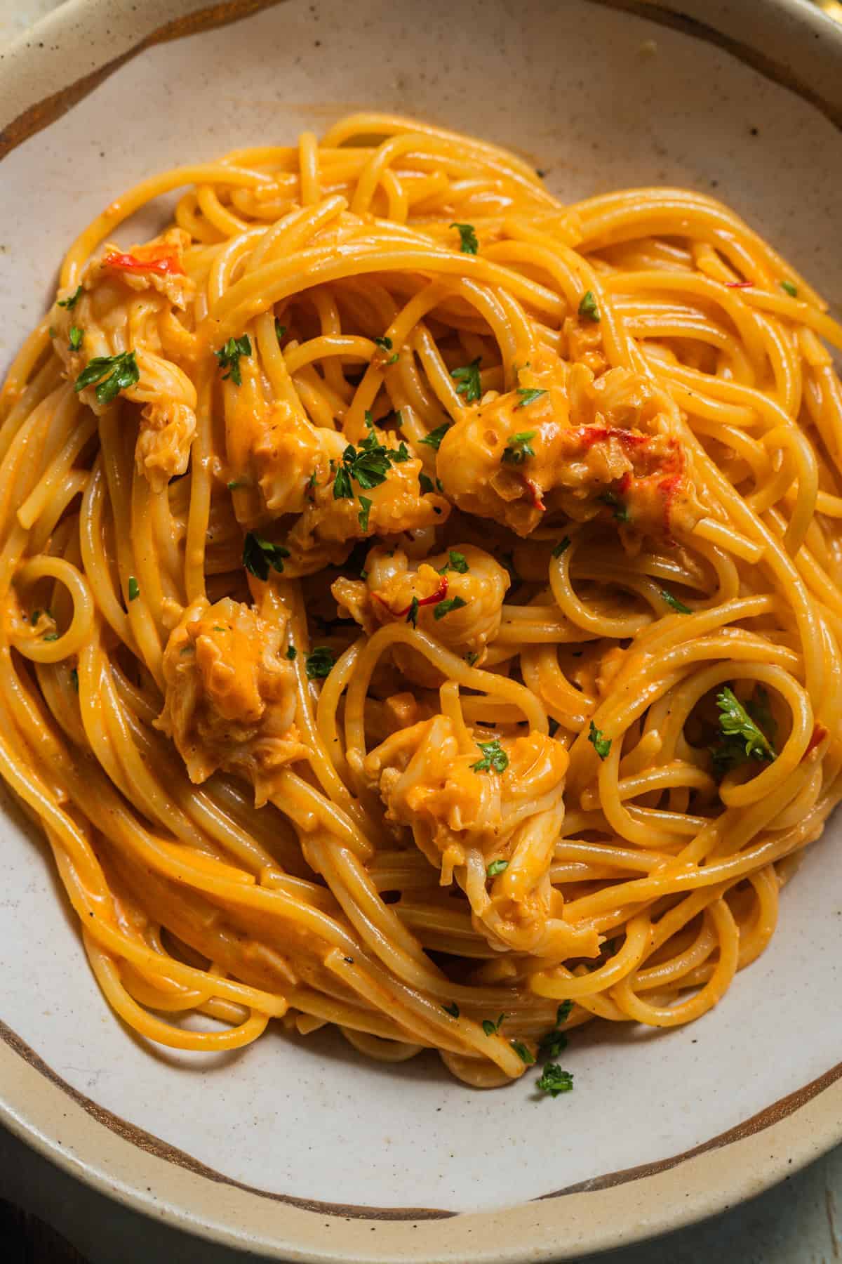 A bowl of pasta coated in an orange cream sauce with bits of lobster and fresh parsley on top.