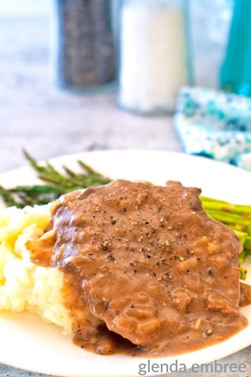 Crock pot cube steak on a white plate with mashed potatoes and asparagus.