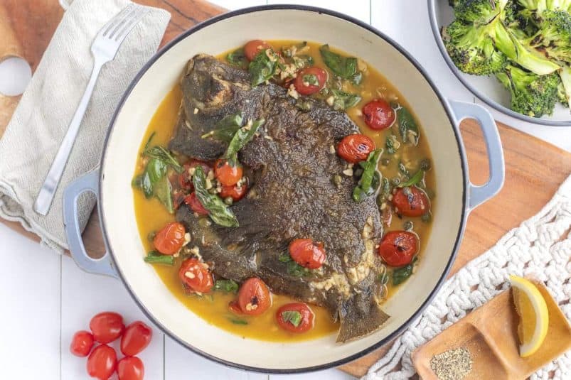 Whole baked flounder in a lemon and basil sauce in a cast iron dish.