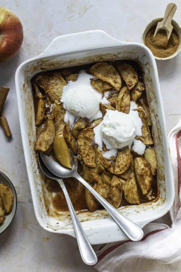 Ceramic baking dish filled with baked apples with cinnamon and topped with ice cream.