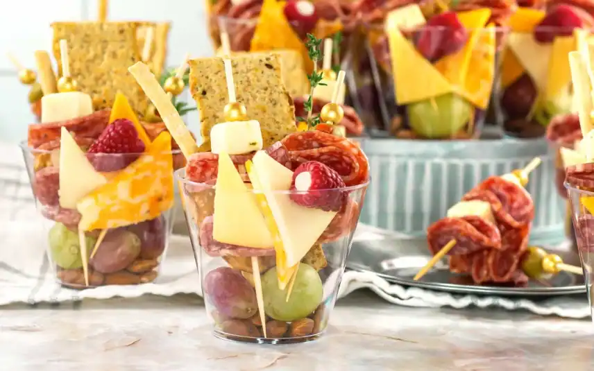 Charcuterie cups on kitchen counter with extra meat skewers on a plate.