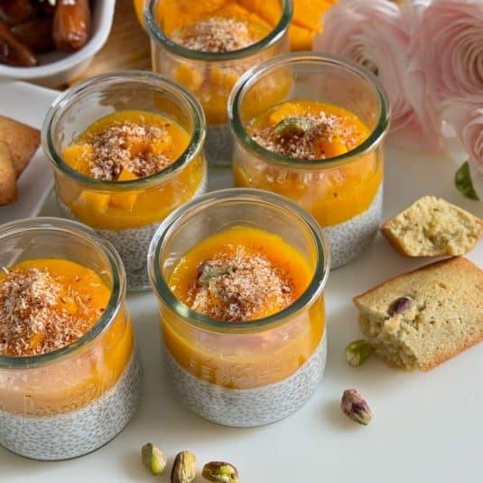 Glass pots with coconut chia pudding topped with mango sauce, mango chunks and dates.