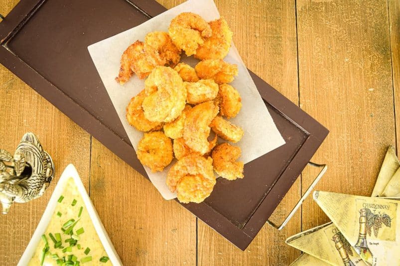 Breaded coconut shrimp on parchment lined serving tray with curry dip on the side.