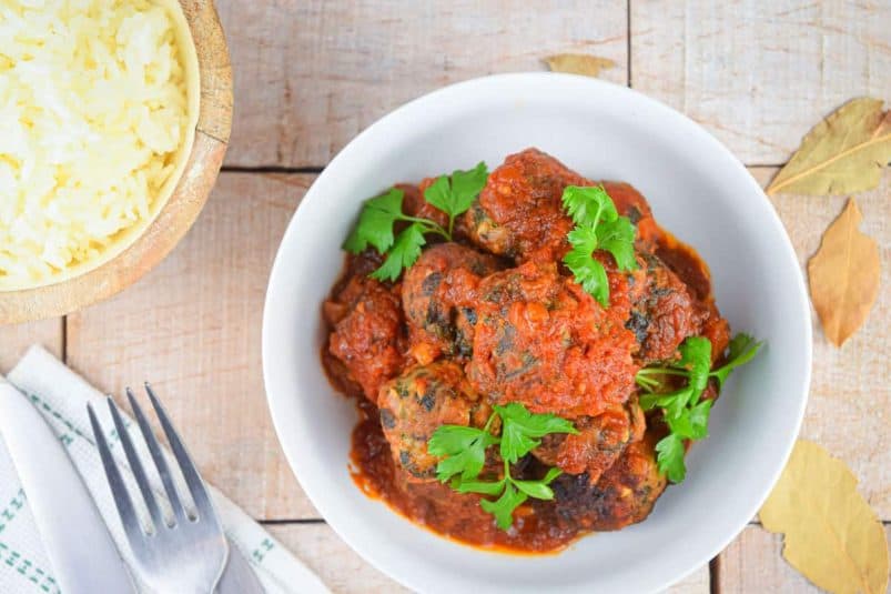 Turkey meatballs in tomato sauce in bowl with rice on the side.
