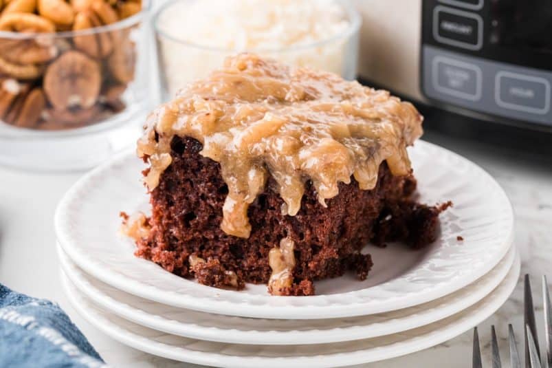 A slice of slow cooker German chocolate cake on a stack of three white plates.