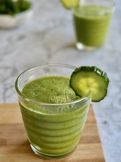 Green kale cooler smoothie in glass with cucumber served on wooden board.