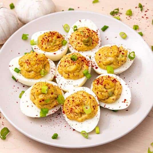 Roasted garlic deviled eggs sprinkled with herbs and pepper on a white plate.