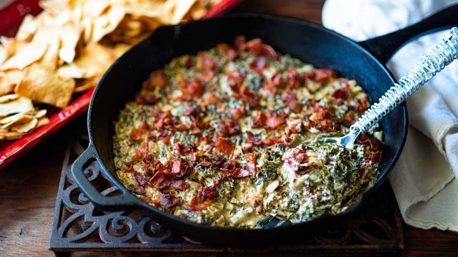 Asiago Kale Bacon Dip being scooped out of a cast iron skillet.