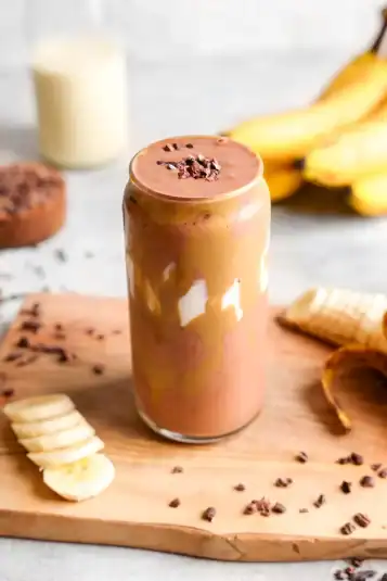 Looking down at the glass of the chocolate banana with sliced bananas and cacao nibs around it.