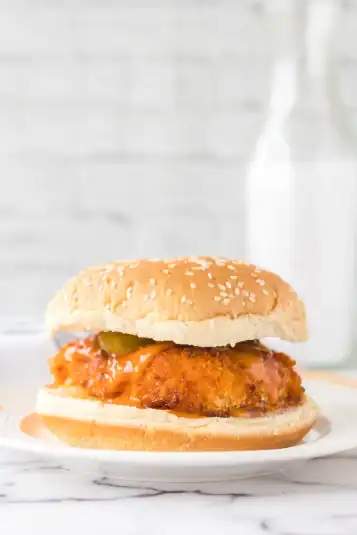 Buffalo Chicken breast on sesame seed bun with sliced pickles.