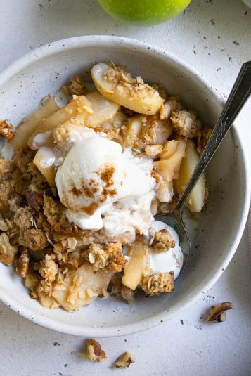 Shallow serving bowl filled with apple crisp and topped with melting scoop of vanilla ice cream.