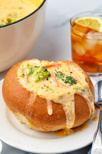 Bread bowl with Broccoli Cheddar Soup Recipe in it with drink and pot in background.