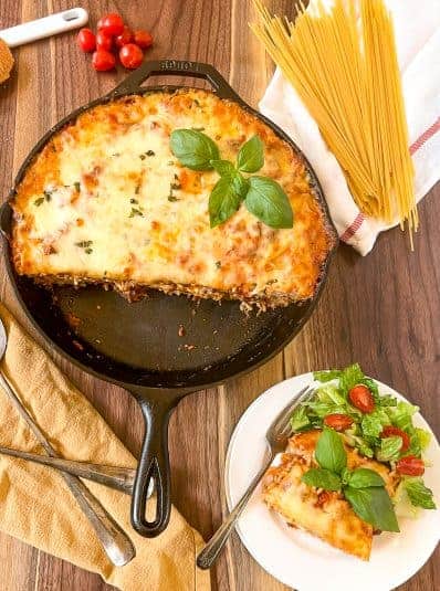 A slice of the cooked pasta has been plated on a white plate with a green salad, the remaining pasta is in the skillet.