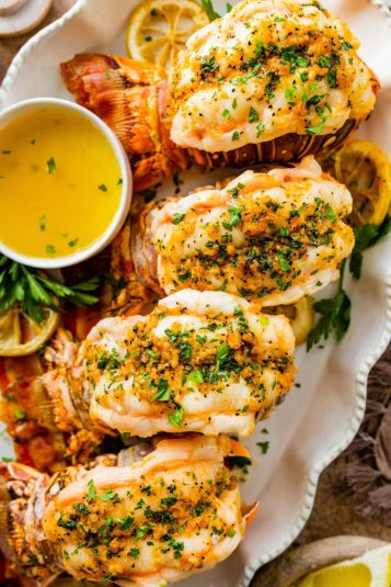 Best Baked lobster tails on a white serving platter with extra melted butter and lemon wedges for serving.
