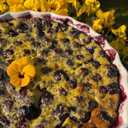 Blueberry clafoutis dessert with lemon and yellow edible pansies.