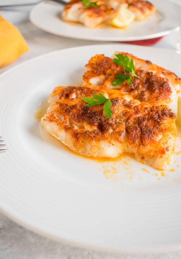 Cooked cod on plate with seasoning and parsley.