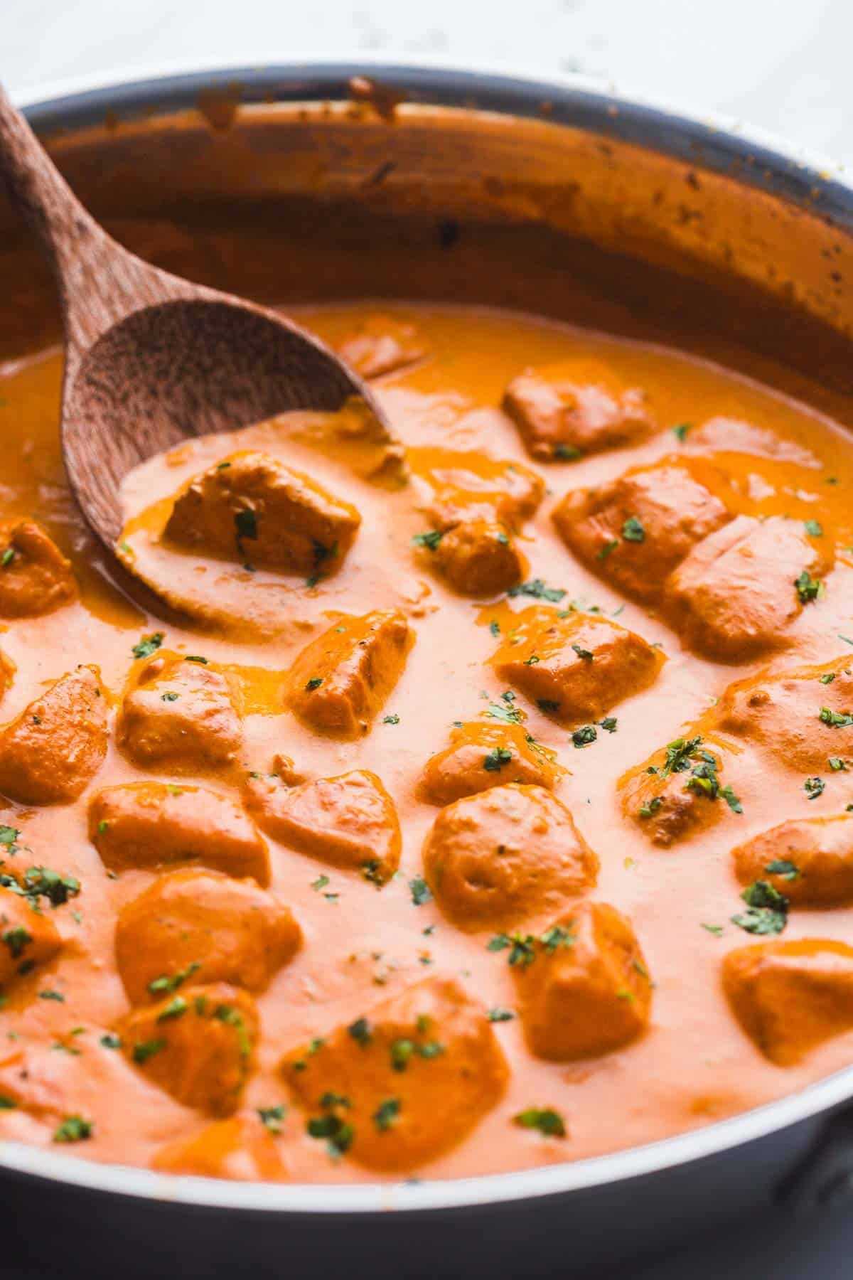A pan with butter chicken and a wooden serving spoon.