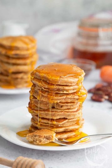 A stack of Carrot cake pancakes on a white plate with a fork at the front topped with honey.