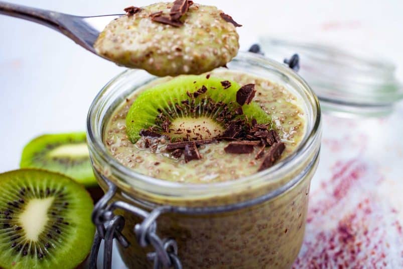 A cup filled with kiwi chia pudding topped with a slice of fresh kiwi fruit and shaved chocolate.