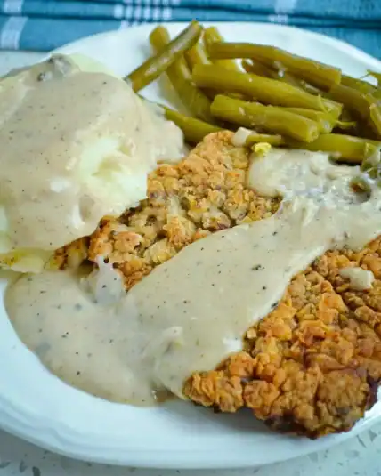 Tender cube steak is double-breaded, fried to golden perfection, and smothered in a creamy flour and milk-based gravy made from the pan drippings.
