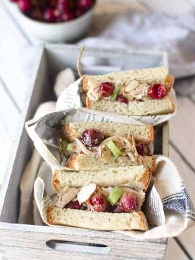 Overhead view of chicken salad with roasted grape sandwiches wrapped in deli paper placed in a grey box.