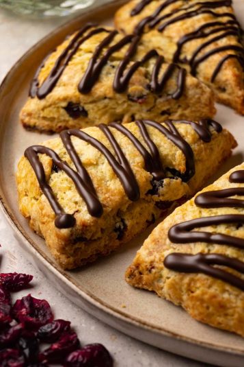 Scones with cranberries and chocolate glaze on a plate. Dried cranberries are lying around the plate.