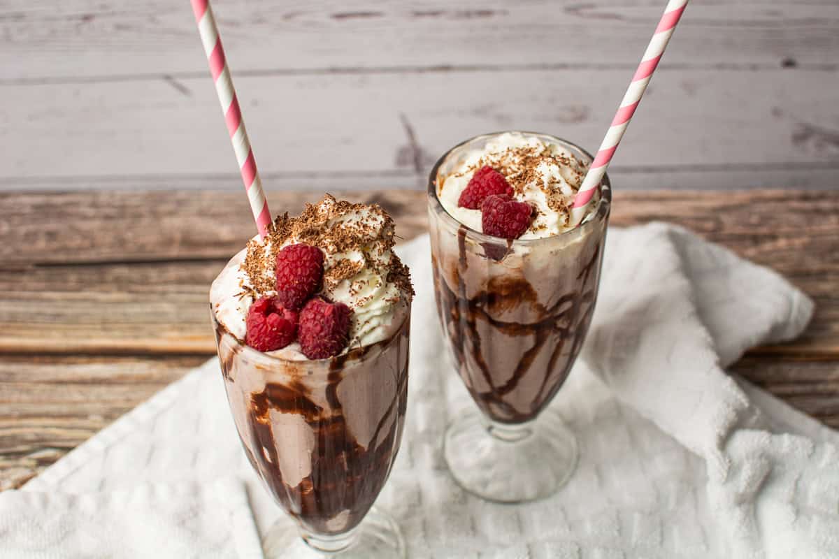 Ice cream, milk, chocolate, and raspberries blended into a shake and served in glasses.