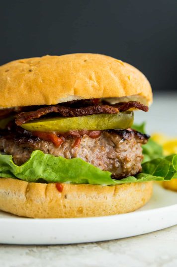A homemade duck burger in a bun with lettuce, pickles, bacon and ketchup.