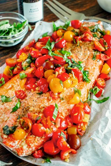 A photo of a side of cooked salmon topped with tomatoes and fresh basil.