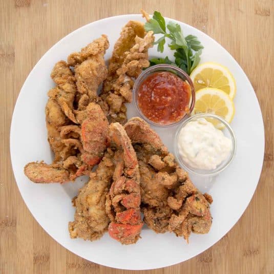 Fried lobster tails on a white plate with lemon slices, cocktail sauce and tartar sauce.