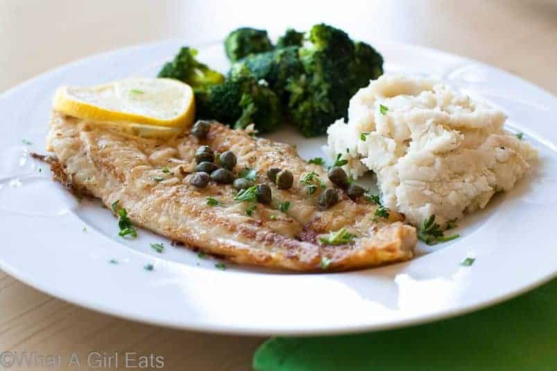 Dover Sole on a white plate with mashed potatoes and broccoli.