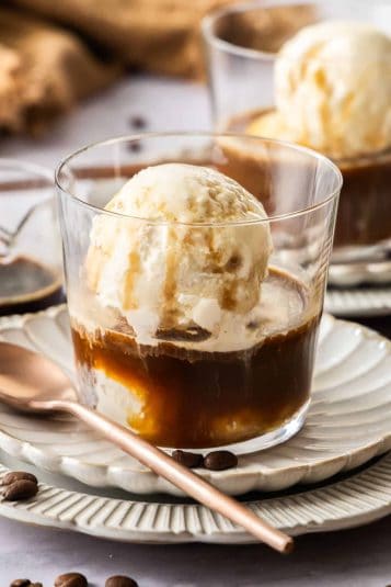 Two glasses with Affogato - coffee, liqueur and ice cream - each sitting on a white fluted saucer, with a bronze spoon.