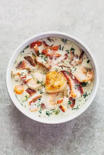 A bowl of creamy seafood soup topped with a pan seared scallop.