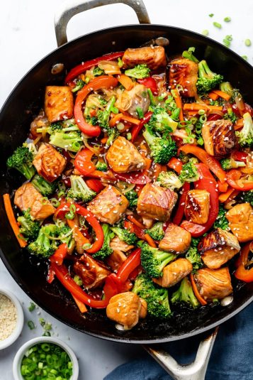 Salmon and vegetables in a stir fry pan cooked and topped with sesame seeds.