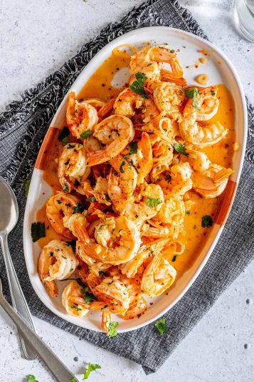 Low carb Shrimp Scampi recipe cooked on a on a plate with fresh parsley, shallots, cooked garlic cloves and shrimp scampi sauce.