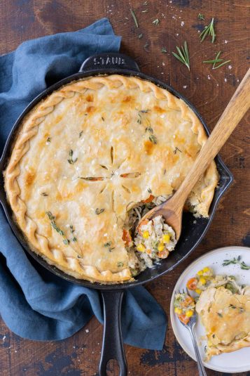 A wooden spoon scoops a serving of Skillet Chicken Pot Pie onto a plate.