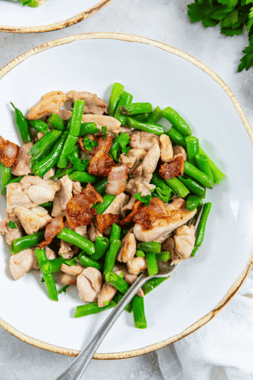 Skillet Chicken Thighs, Bacon, and Green Beans in a white bowl with a fork.