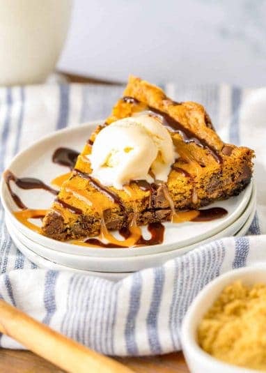 Slow Cooker Chocolate Chip Cookie cut into triangular piece and served with a scoop of vanilla ice cream, chocolate syrup, and caramel syrup.
