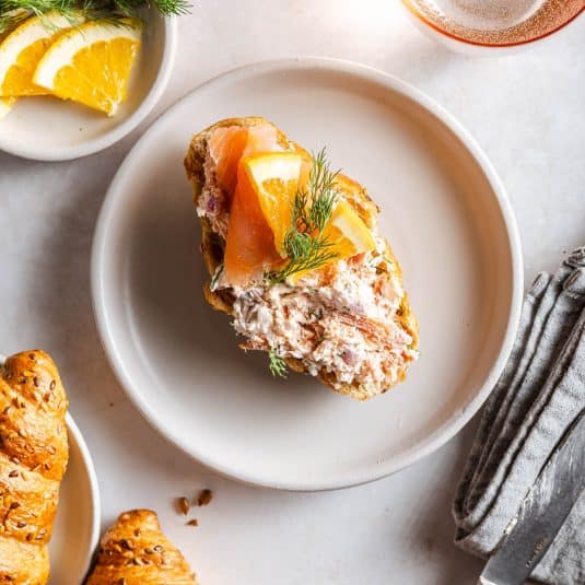 A greige plate with a croissant topped with a salmon spread and salmon-lemon garnish.