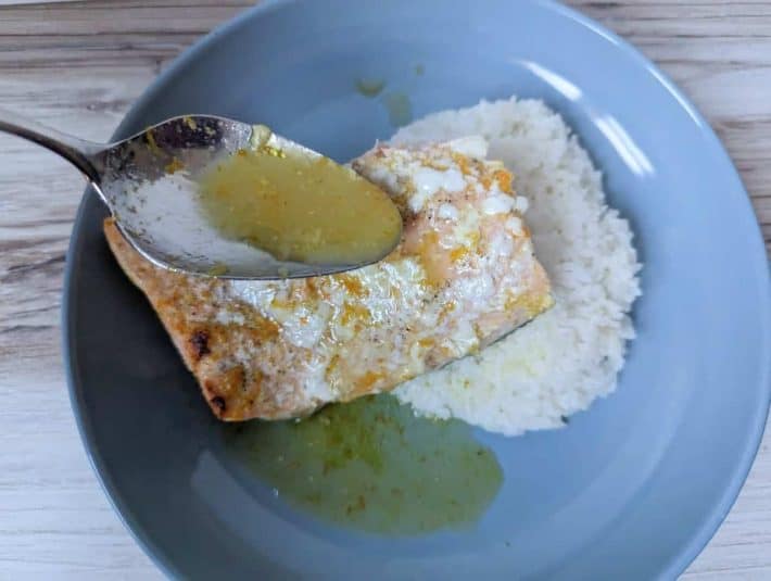 Image shows a fork holding a bite of an Asian glazed salmon with the remaining serving in the background.