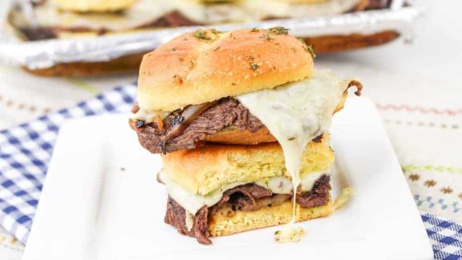 Stacked roast beef and melted cheese sandwich on a square white plate with a toasted bun.