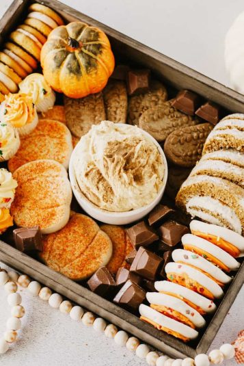 Wooden tray filled with pumpkin cream cheese dip, cookies, candies, and fall cupcakes.