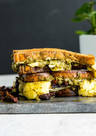 A turkey pesto panini that is cut in half and stacked on a cutting board.