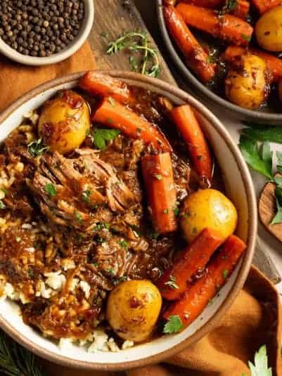 Up close bowl of pot roast over rice with herbs and veggies.