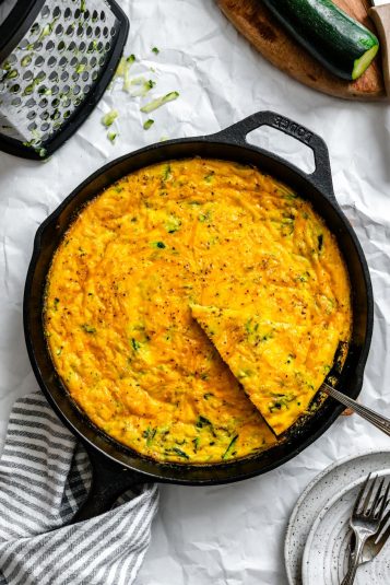 A server removing a piece of zucchini frittata from a cast iron skillet.