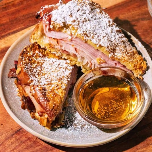 Monte Cristo sandwich cut in half served with a small bowl of maple syrup.