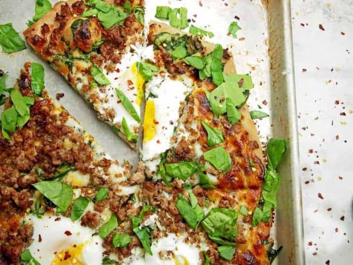 Overhead view of a sliced pizza with drippy eggs, sausage, and spinach on top.
