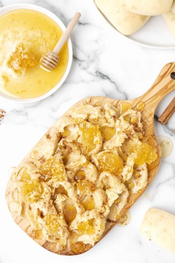 Wood serving board covered with cinnamon honey butter and drizzled with additional honey.