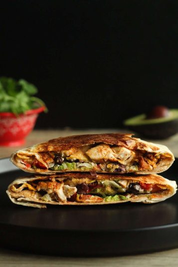 A chicken crunch wrap cut in half and placed on top of the other half with inside exposed on a black plate.