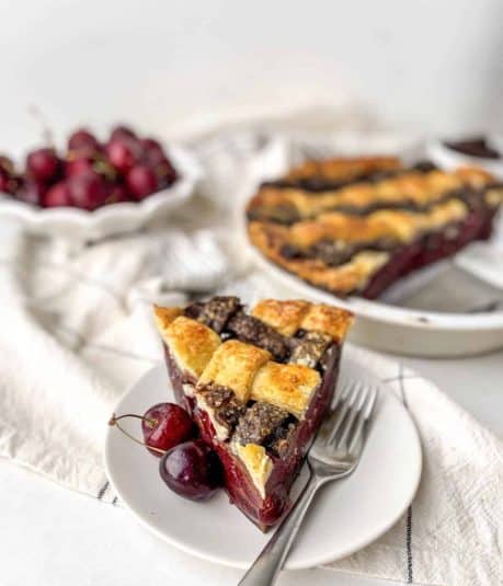 Slice of Chocolate Cherry Pie on a white plate with a bowl of cherries in the background.